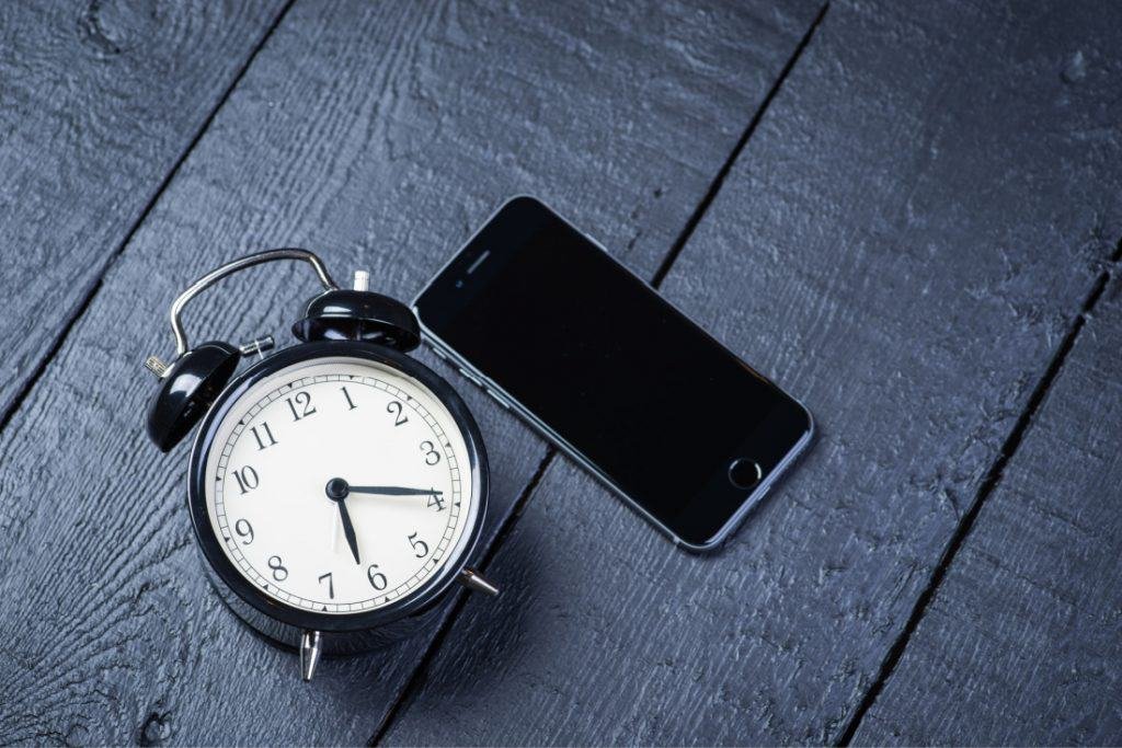 cell phone next to an alarm clock 