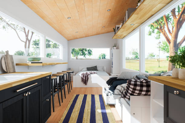 A modern tiny house interior with wood accents, large windows, a kitchen with black cabinets, a breakfast bar with stools, and a small living area with a sofa and cushions—perfect inspiration for small space decor enthusiasts.