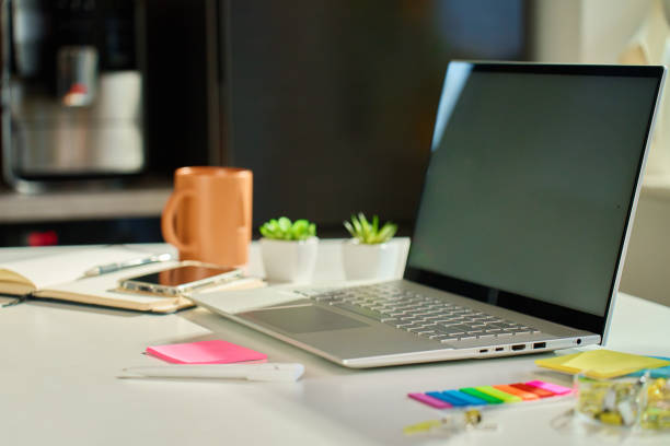 A laptop sits on a white desk with colorful sticky notes, a smartphone, a notebook, two small potted plants, a mug, and office supplies—creating an ideal home office setup that supports work and mental health.