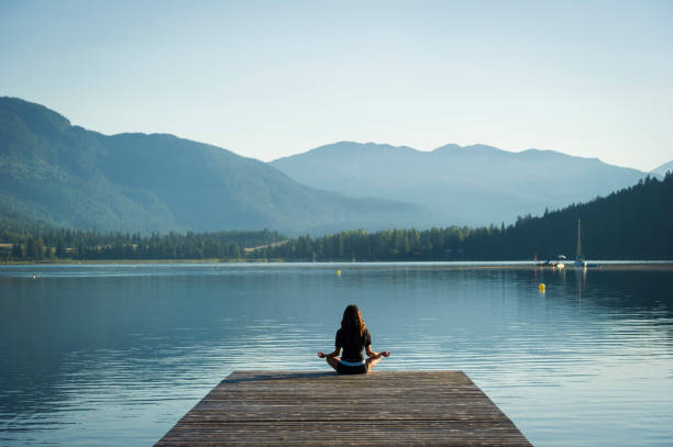 A person sits cross-legged on a dock facing a calm lake, surrounded by mountains under a clear sky—finding peace with quick mindfulness after a busy day.