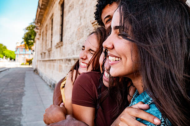 Three friends stand outside near a stone building, hugging and smiling close together on a sunny day, feeling empowered by their friendship and shared boundaries.