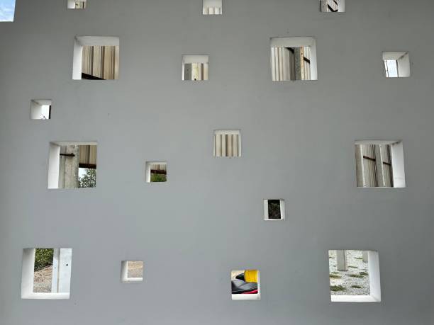 White gratitude wall with multiple square cutouts of various sizes, allowing views of the outdoor area and structures behind it.